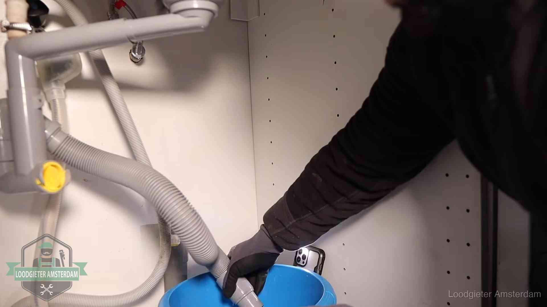 Afvoerslang loopt leeg in een emmer onder de gootsteen in Amsterdam, een klus die je zelf kunt doen