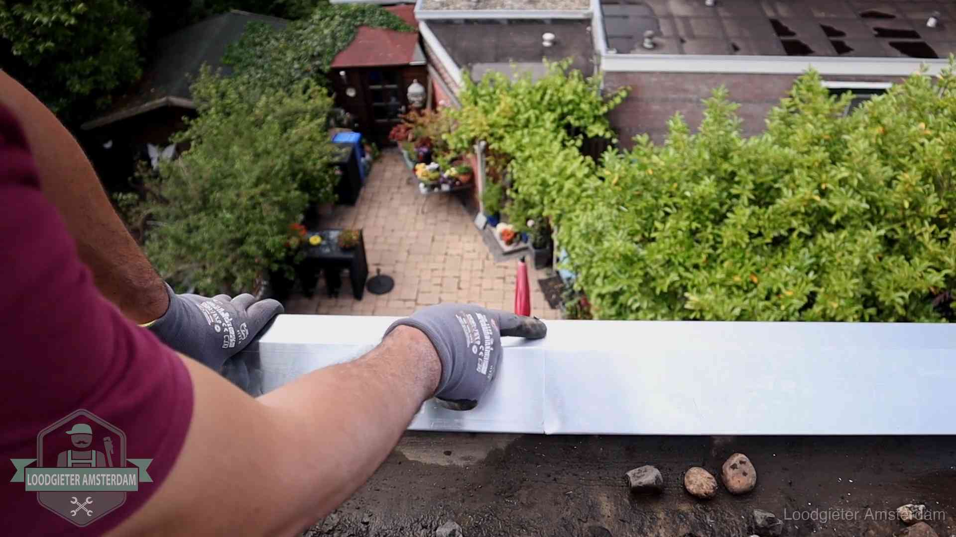 Vakman plaatst een daktrim op de dakrand van een woning in Amsterdam