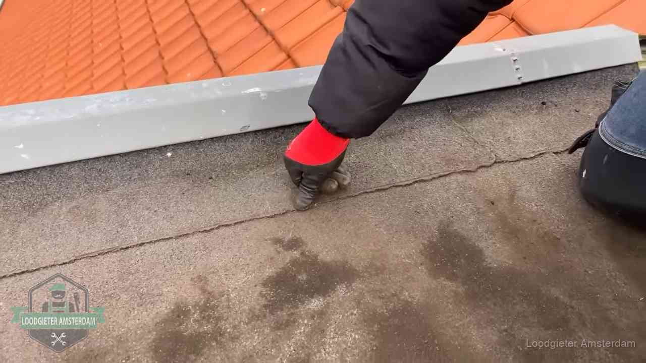 Vakman wijst een naad met vochtplekken aan op een bitumen plat dak in Amsterdam