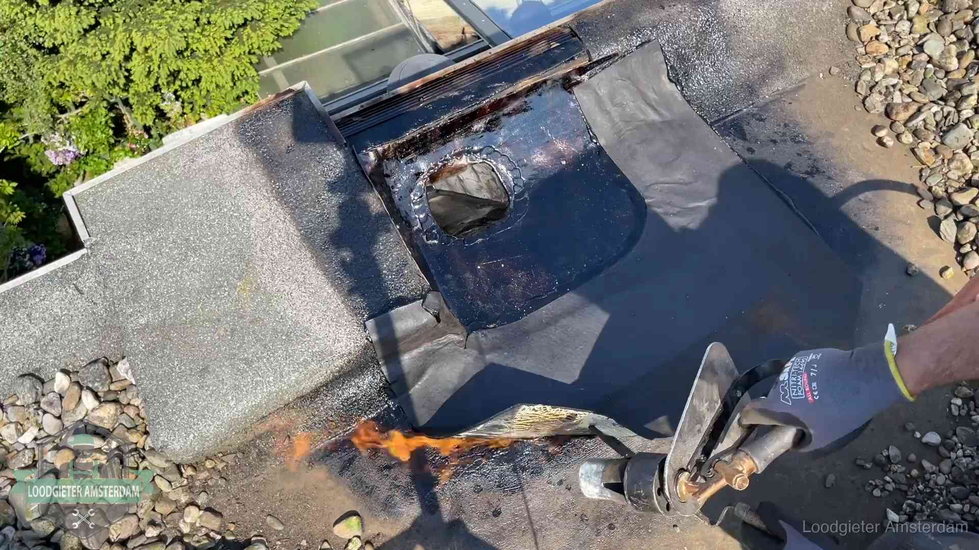 Dakdekker brandt bitumen rond een doorvoer tijdens een daklekkage-reparatie in Amsterdam
