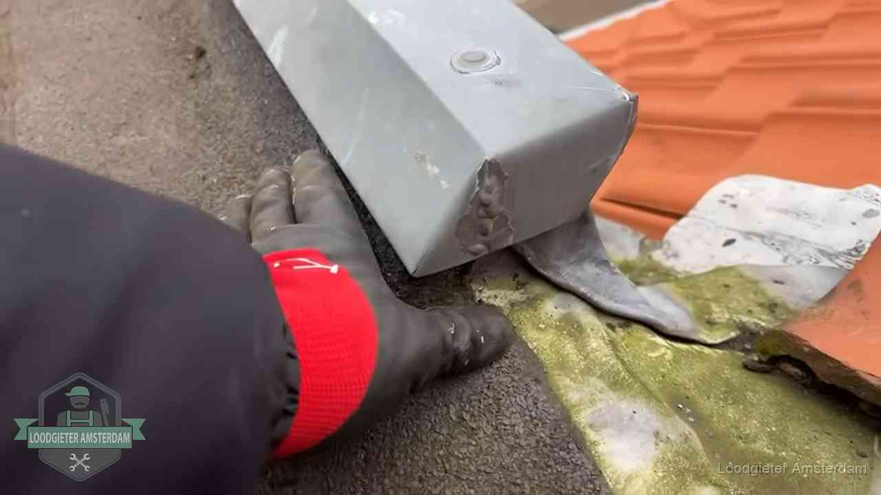 Controle van een zinken hemelwaterafvoer met loodslab bij dakpannen in Amsterdam