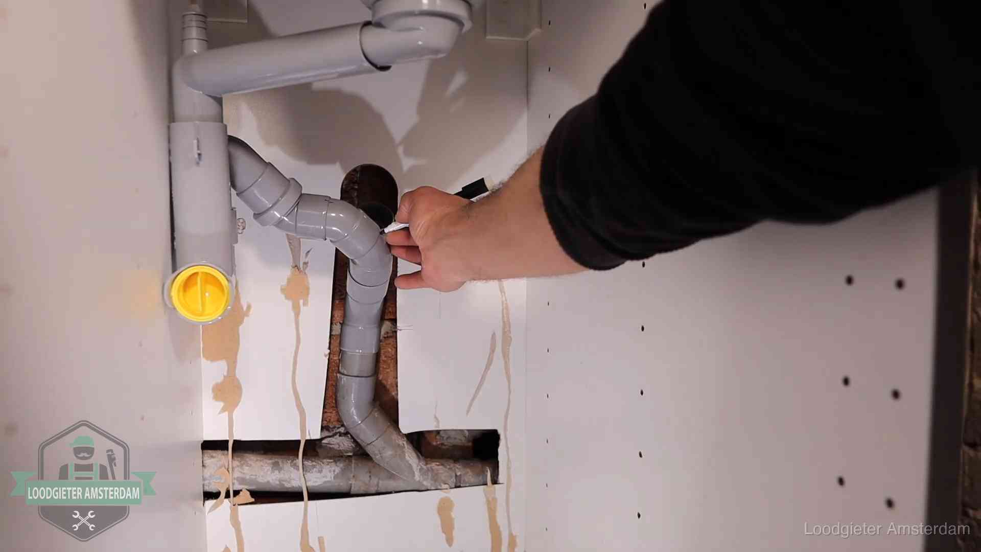 Loodgieter markeert een pvc-afvoerbuis onder een gootsteen in Amsterdam