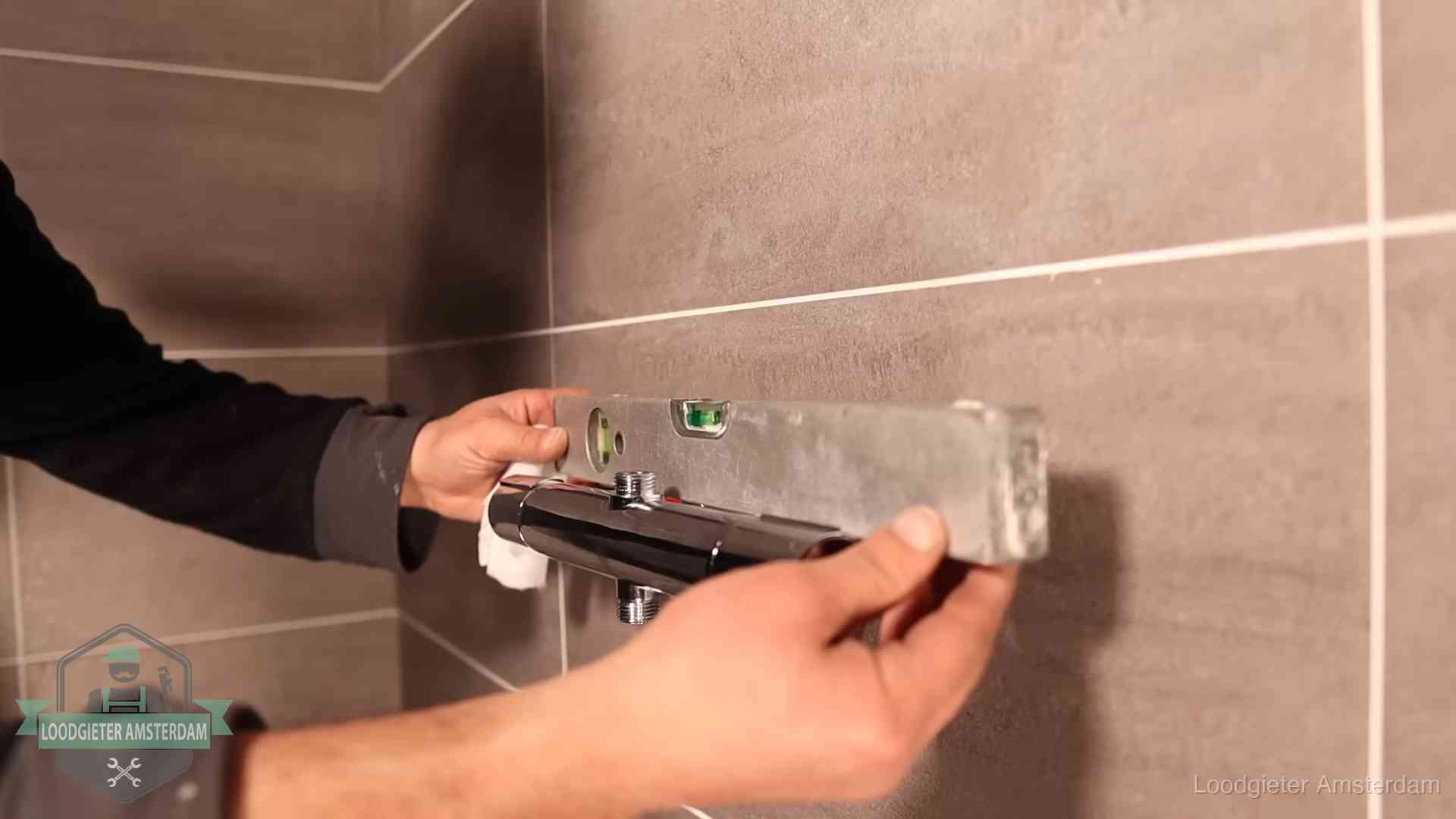 Loodgieter lijnt een douchekraan uit met een waterpas in een woning in Amsterdam