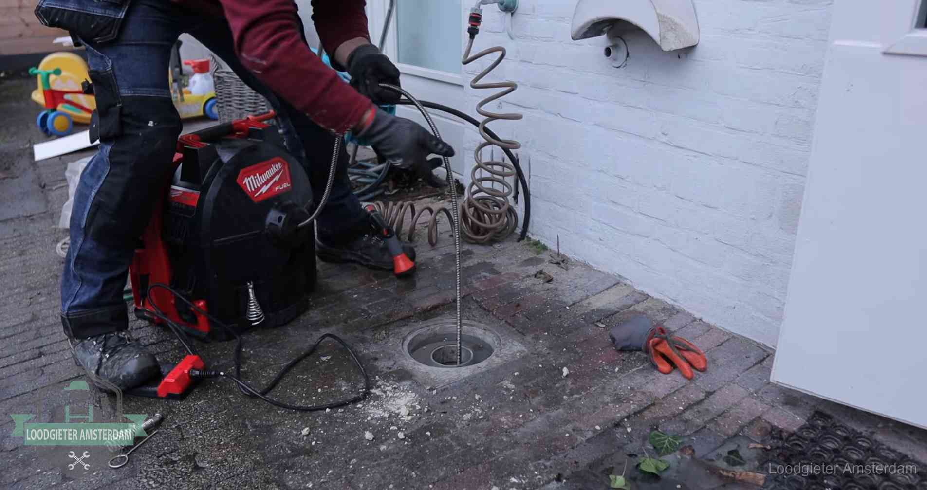 Ontstoppingsputje in de bestrating naast de gevel van een woning in Amsterdam