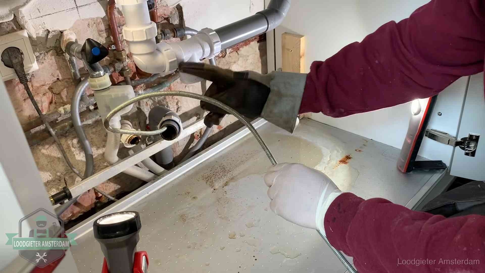 Ontstoppingsveer gaat in een geopende sifonaansluiting onder het aanrecht in Amsterdam