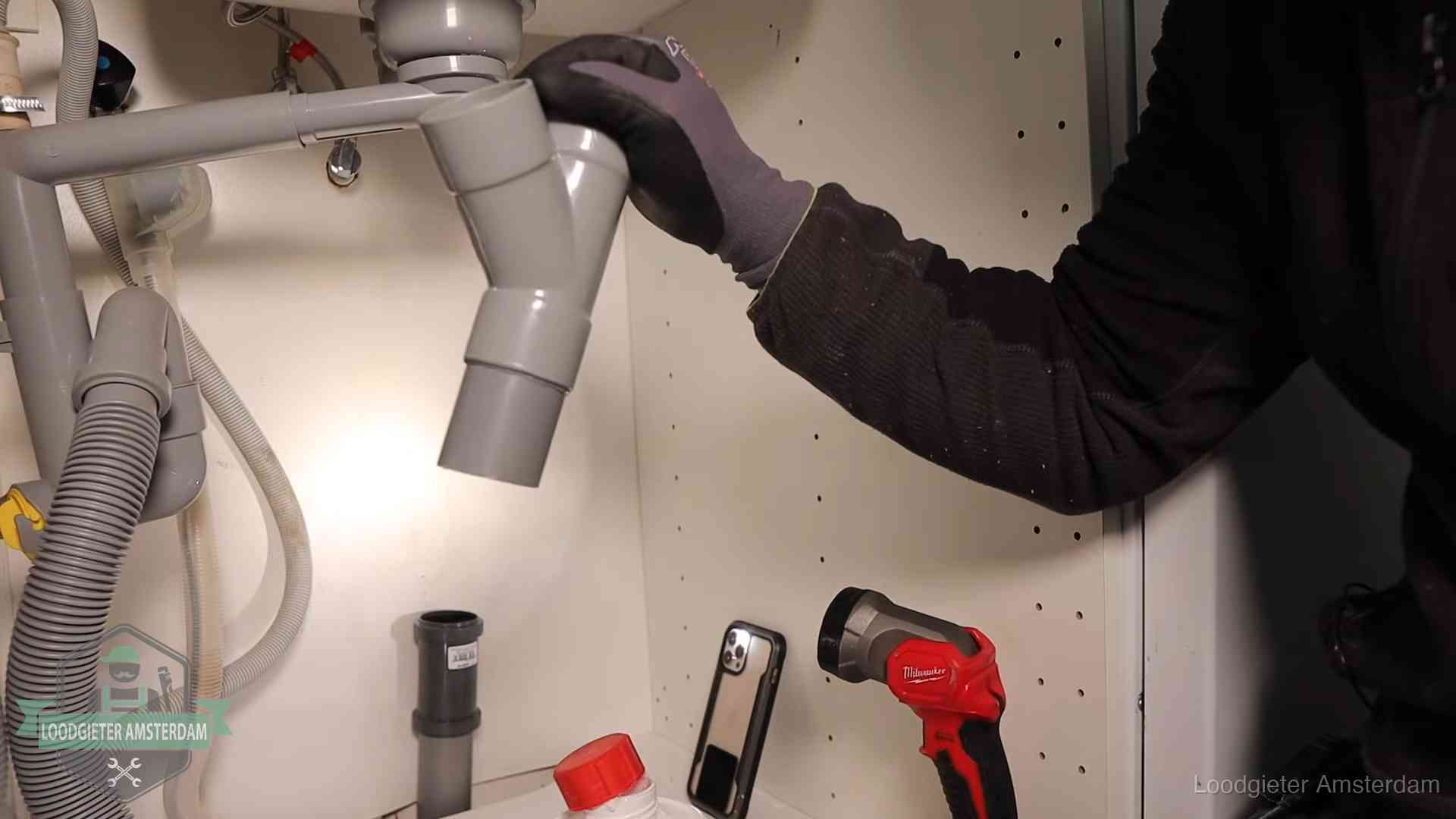 Loodgieter demonteert het sifon- en afvoerwerk onder een gootsteen in Amsterdam bij stankklachten