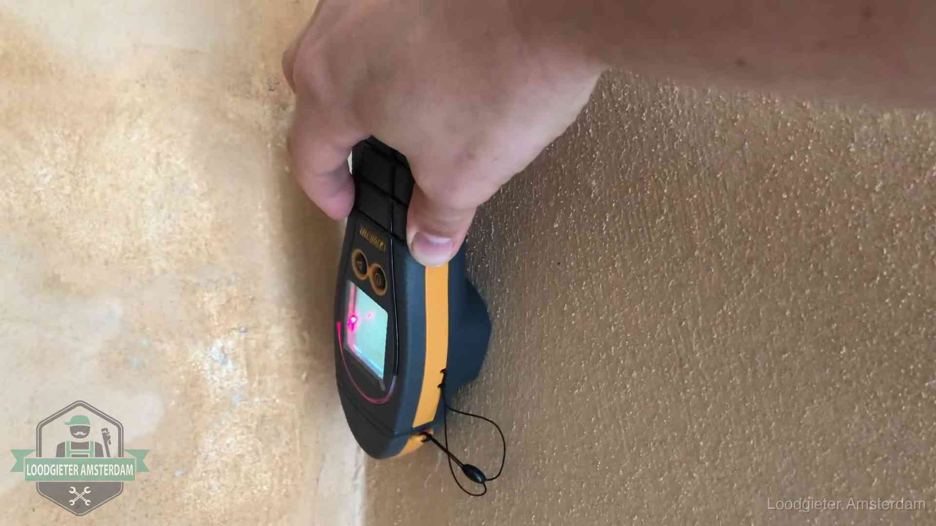 Vochtmeter tegen een muur met vochtplekken tijdens het opsporen van een daklekkage in Amsterdam