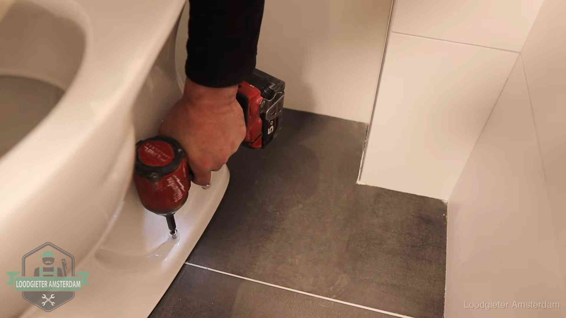 Loodgieter zet de voet van een wc-pot vast op de tegelvloer in Amsterdam